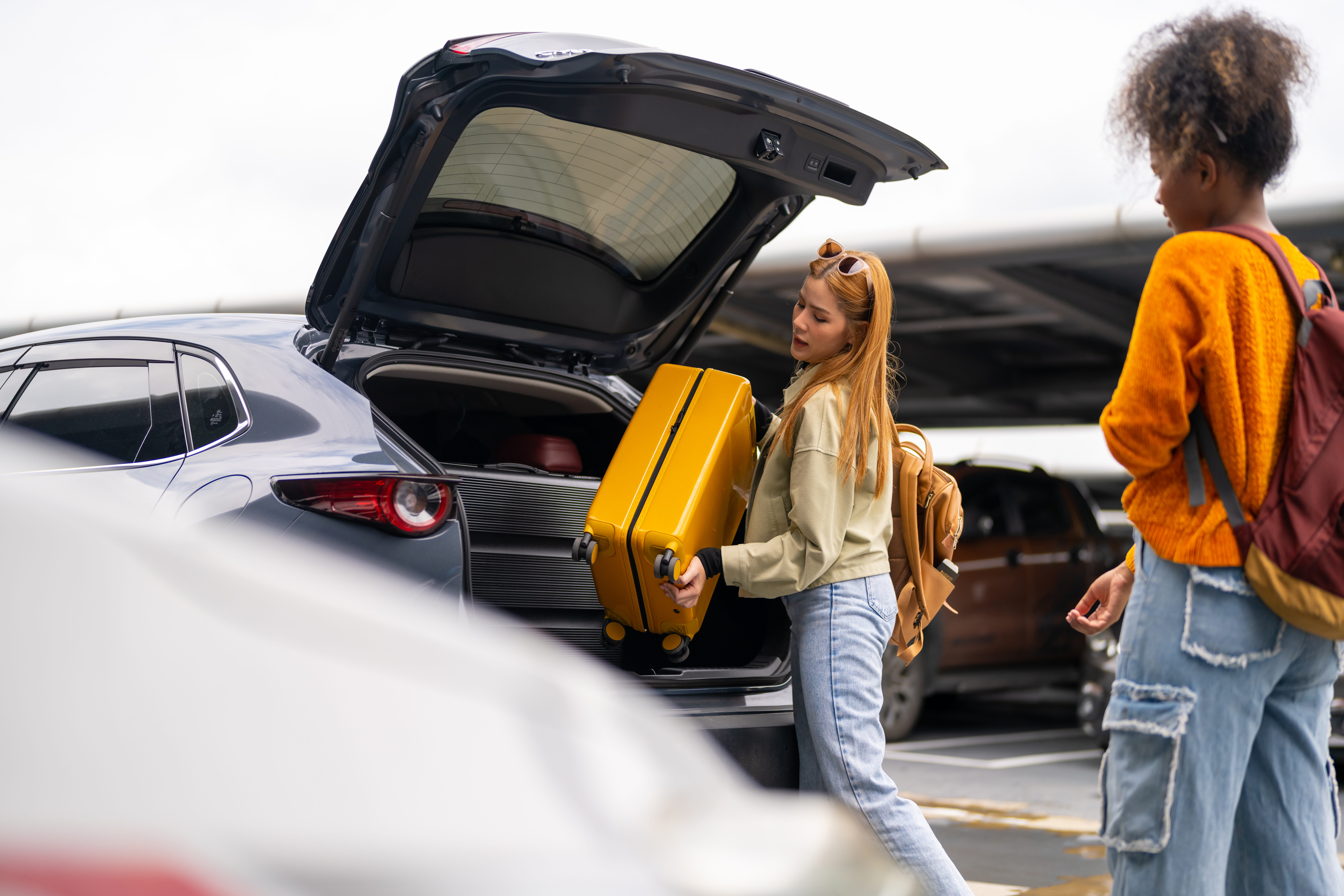 happy woman passenger with passport travel by air transportation. woman friends taking off luggage from car trunk in airport parking and walking to airline check in counter at airport terminal.